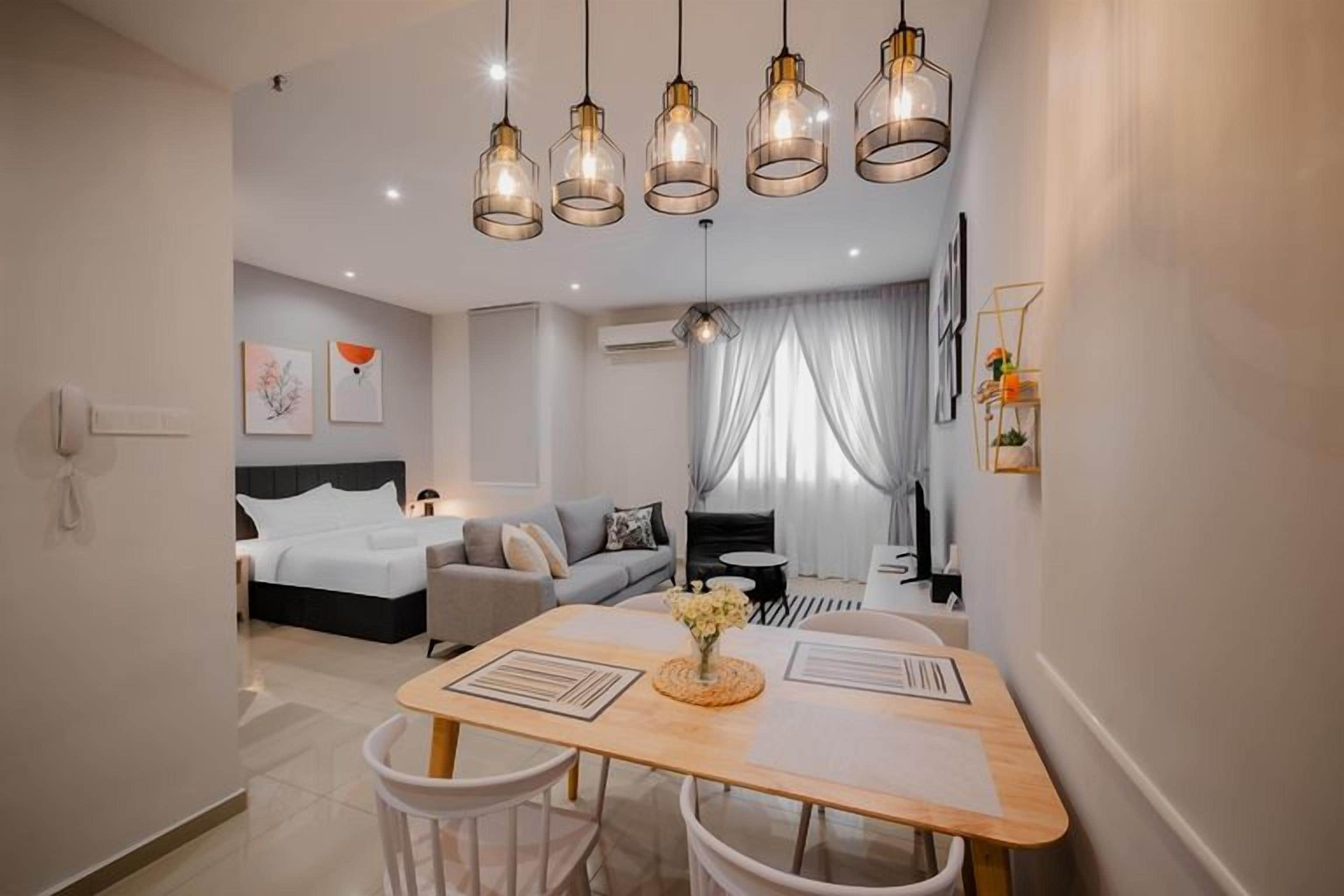 A modern hotel room with a dining area, a bed with a headboard, and a view of the city.