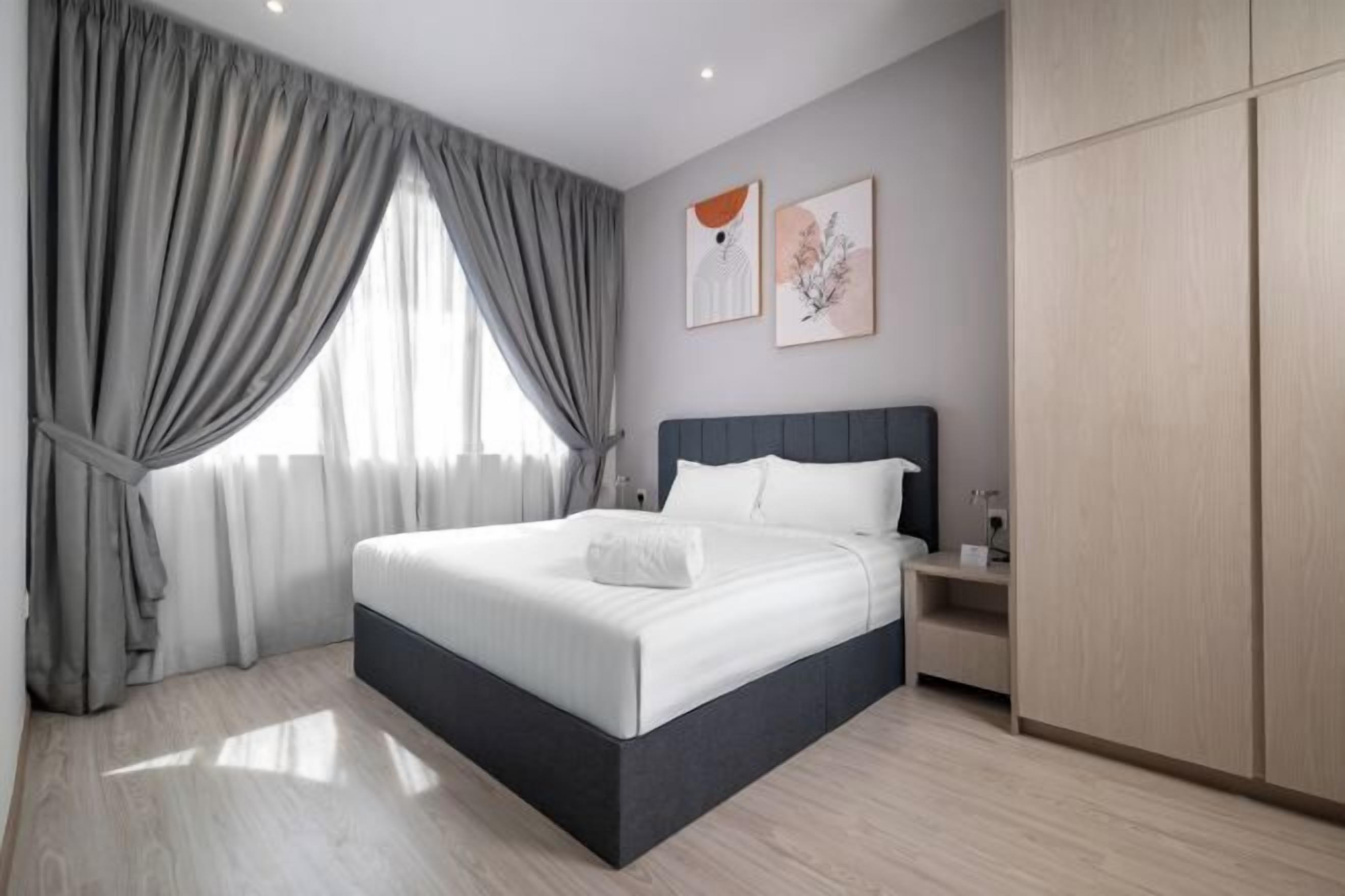 A modern bedroom with a large bed, grey curtains, and two framed artworks on the wall.
