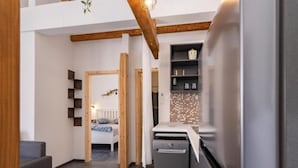 A modern kitchen with a built-in oven and a refrigerator, a dining area with a grey sofa, and a bedroom with a white bed and patterned bedding. - Apartment Sea&sunset View (Novalja)
