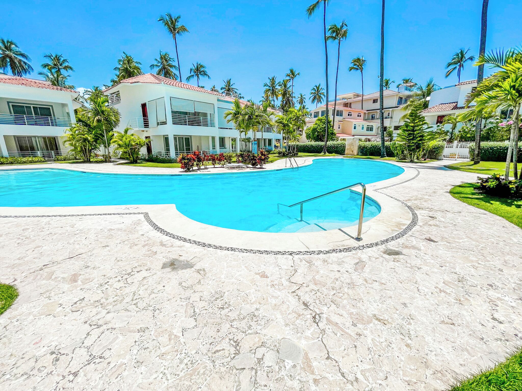 A swimming pool with a curved edge, surrounded by a paved walkway.