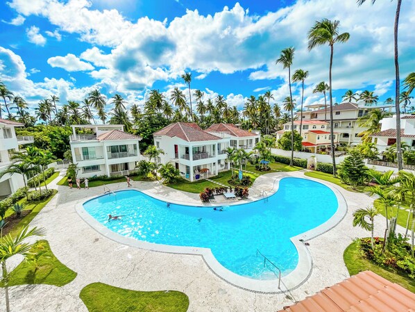 A resort with a large swimming pool, multiple-story buildings, and palm trees. - BEACH FUN AND LIFE (Punta Cana)
