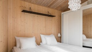 A bedroom with wooden walls, a bed with white bedding, a bedside lamp, and a mirror on the wall.