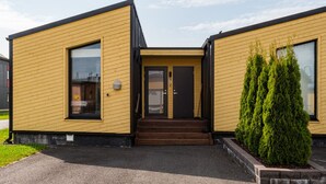 A modern two-story building with a yellow exterior and black trim. It features a front entrance with a set of stairs leading up to a door marked with the number 12.