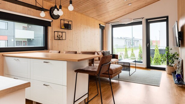A modern kitchen with a wooden ceiling, a large island, and a dining area with a sofa and chairs.