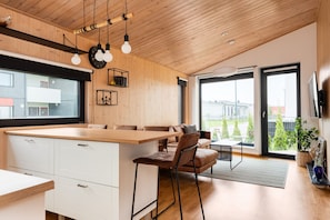 Una cocina moderna con techo de madera, una isla grande y un comedor con sofá y sillas.