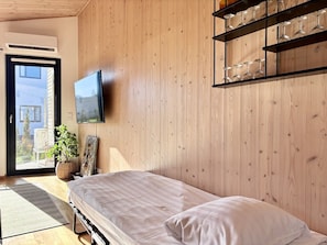 A bedroom with a bed, a TV mounted on the wall, a wooden wall, and a balcony with a plant. - Borg Karjaranta | Sauna · A/C · Terrace · Grill (Pori)