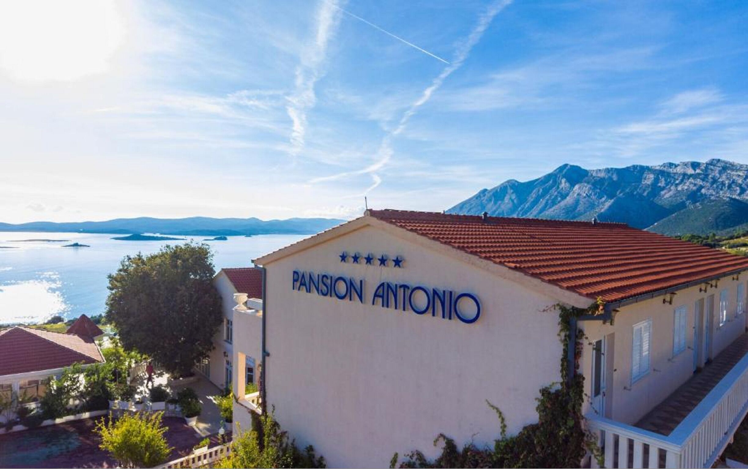 Un edificio con el letrero "Pansion Antonio" y vista a un lago y montañas al fondo.