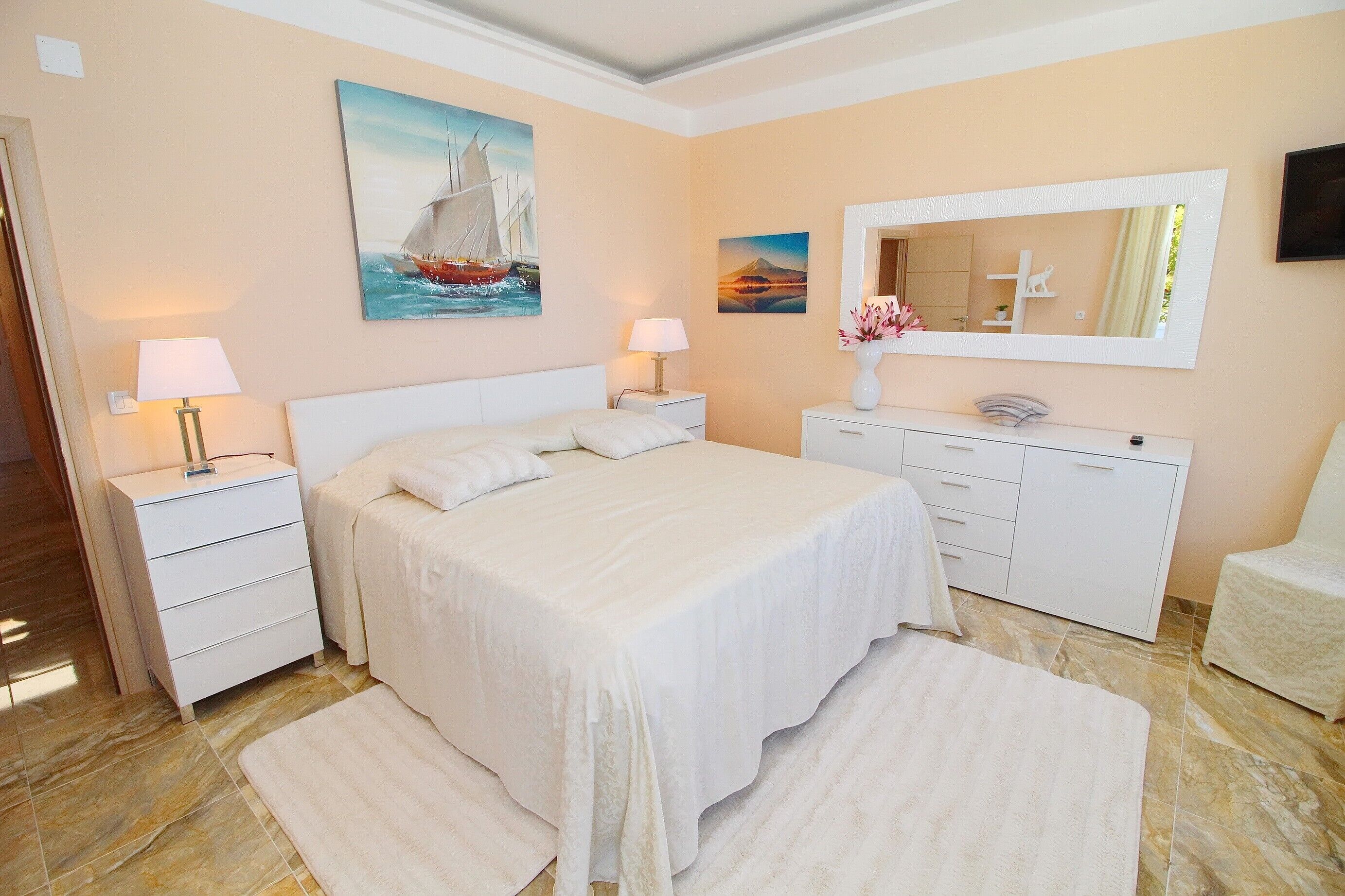 A bedroom with a large bed, two bedside tables, a dresser, a chair, and a mirror.