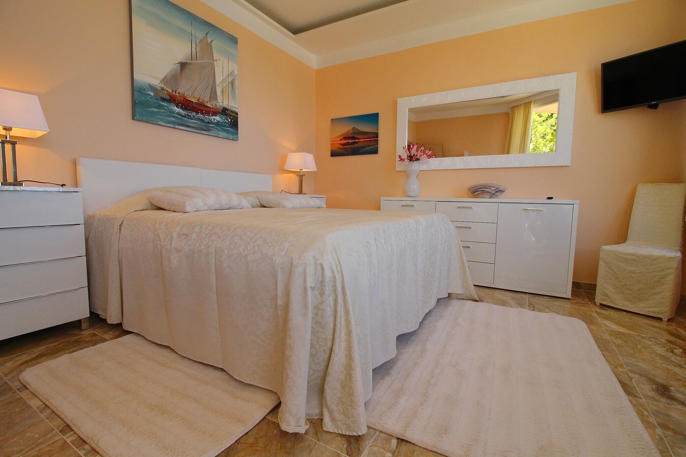A bedroom with a bed, bedside tables, a dresser, a mirror, and a TV.
