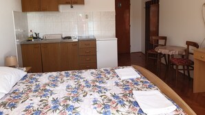 Une chambre comprenant un lit, un petit coin cuisine, des placards en bois, une porte et un espace repas avec des chaises et une table.