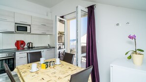 A modern kitchen with a microwave, a dining table set with cups and a coffee pot, and a view of the outdoors through an open door. - Villa Samba - Two Bedroom Apartment with Balcony and Sea View (Mlini)