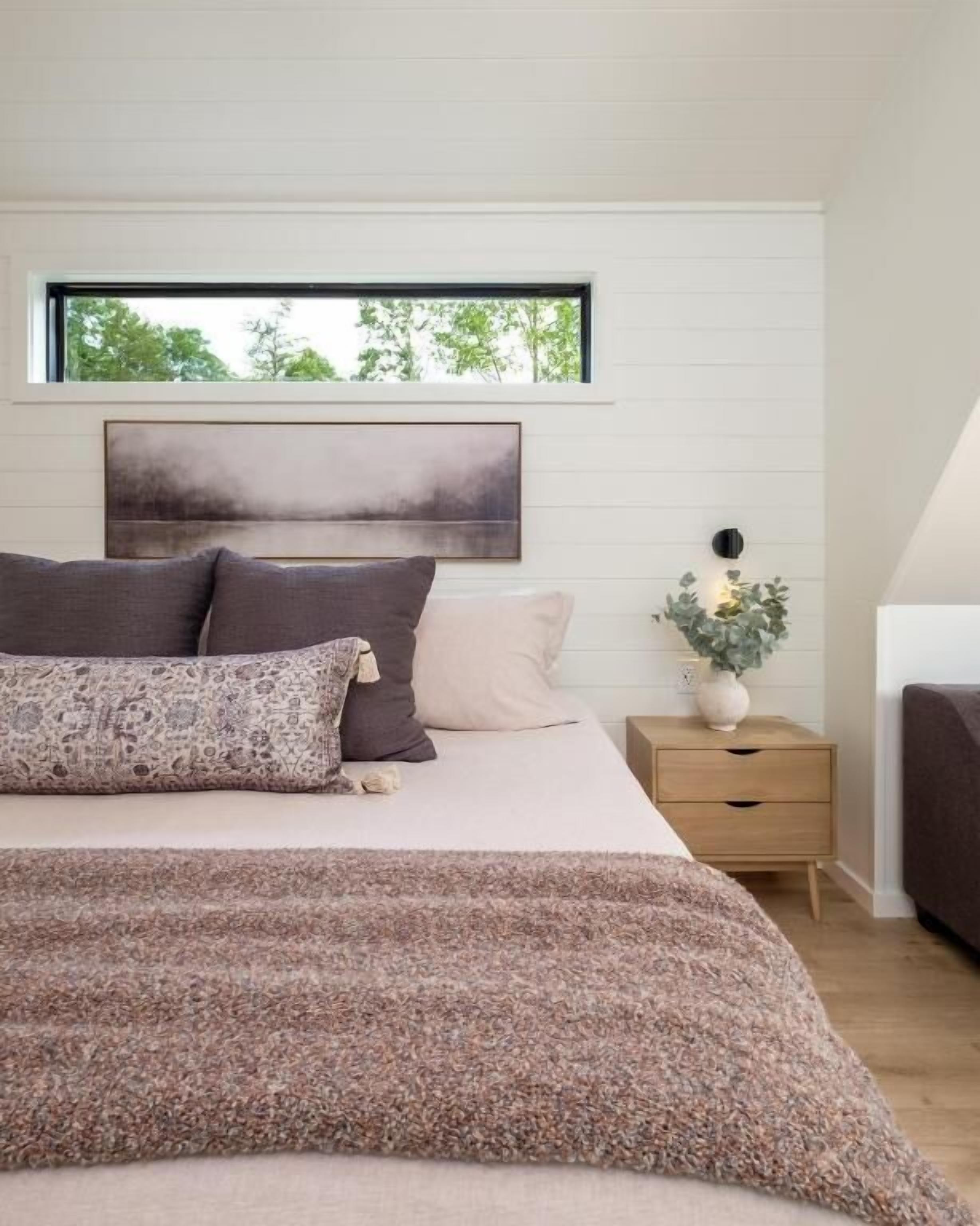 A bedroom with a bed, a nightstand, a window, and a painting on the wall.