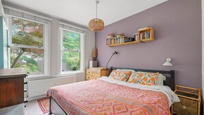 Ein Schlafzimmer mit Bett, Kommode, Fenster, einer Bücherablage und einer Lampe.