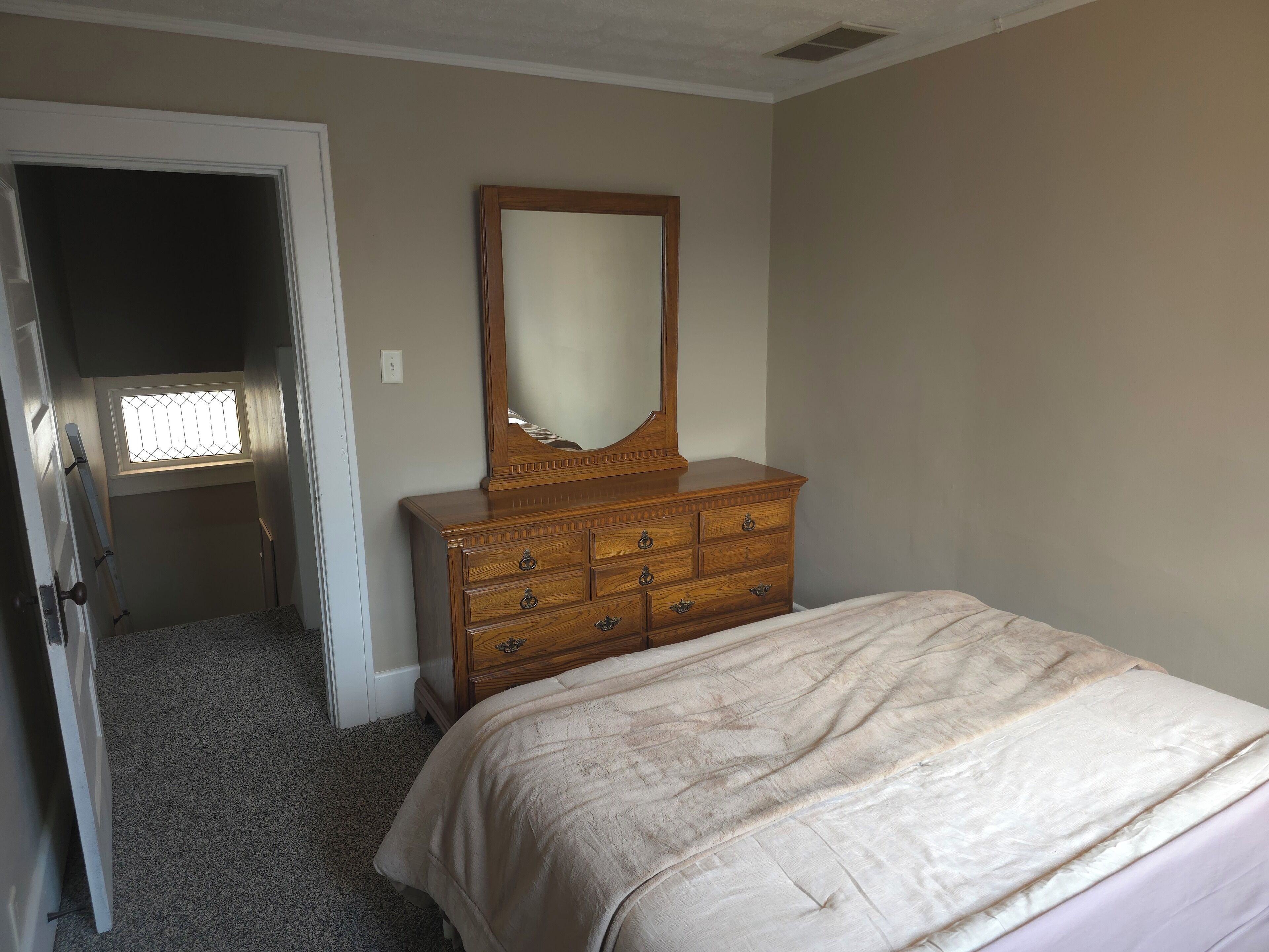 Une chambre à coucher avec un lit, une commode en bois avec des tiroirs, un miroir et une fenêtre.