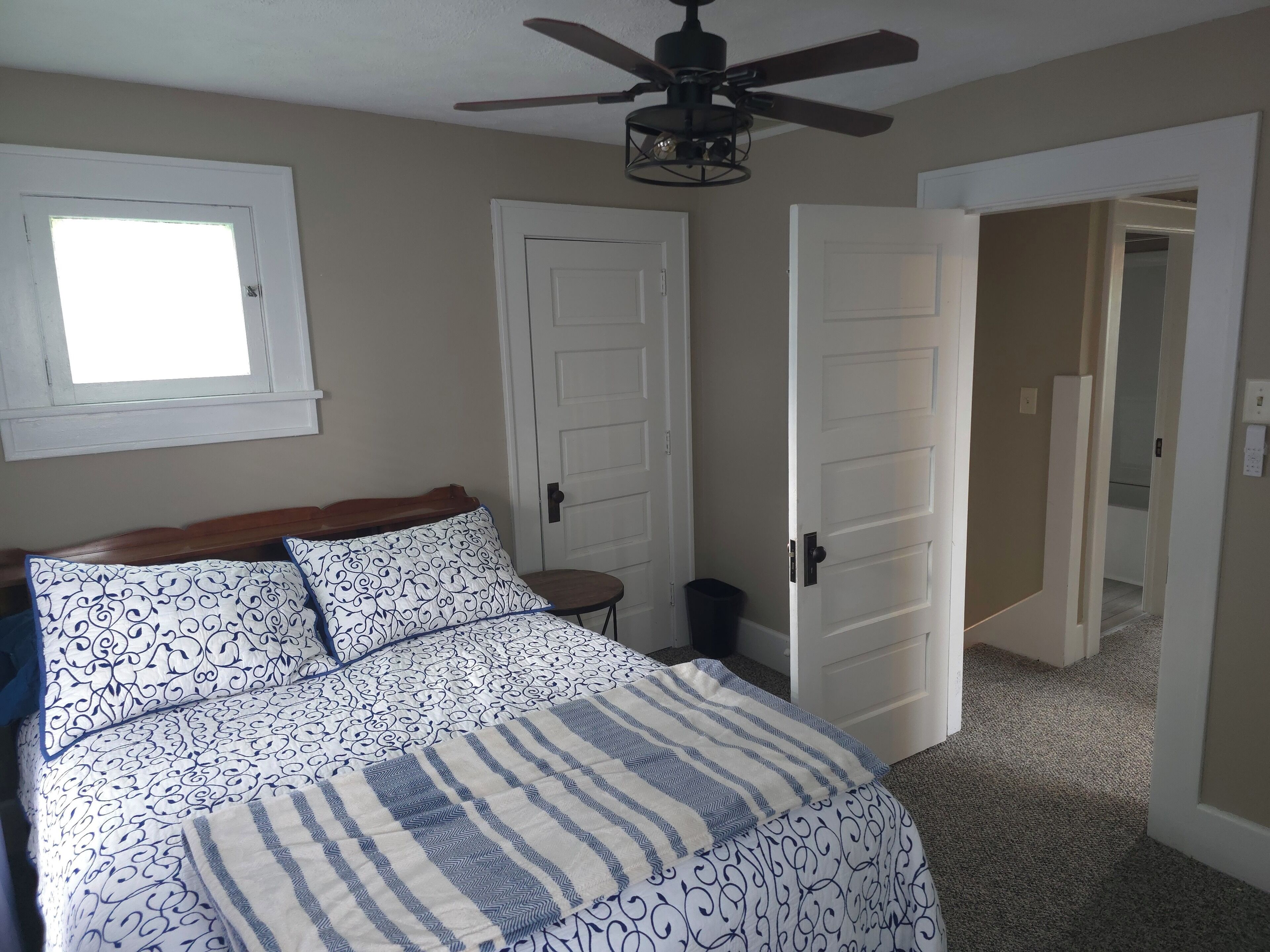 Une chambre à coucher avec un lit, un ventilateur de plafond, une fenêtre et deux portes.