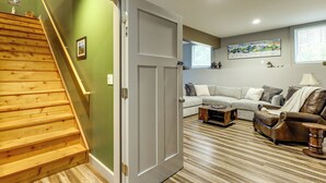 Una escalera conduce a una habitación con pared verde, puerta gris, sofá gris, sillón de cuero marrón y mesa de centro de madera.