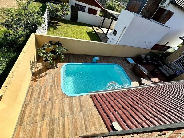 Une piscine sur le toit, dotée d’une terrasse en bois, entourée d’un bâtiment blanc et d’une pelouse verdoyante.