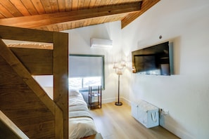 Ein Schlafzimmer mit schrägen Wänden, einem Bett, einem Nachttisch, einer Lampe und einem an der Wand befestigten Fernseher.