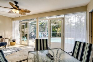 Una habitación con una mesa de vidrio, sillas a rayas, un ventilador de techo y vistas a un área de piscina al aire libre.
