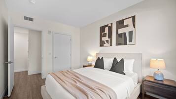 Una habitación de hotel con una cama grande, dos mesitas de noche con lámparas, una puerta y arte abstracto en la pared.