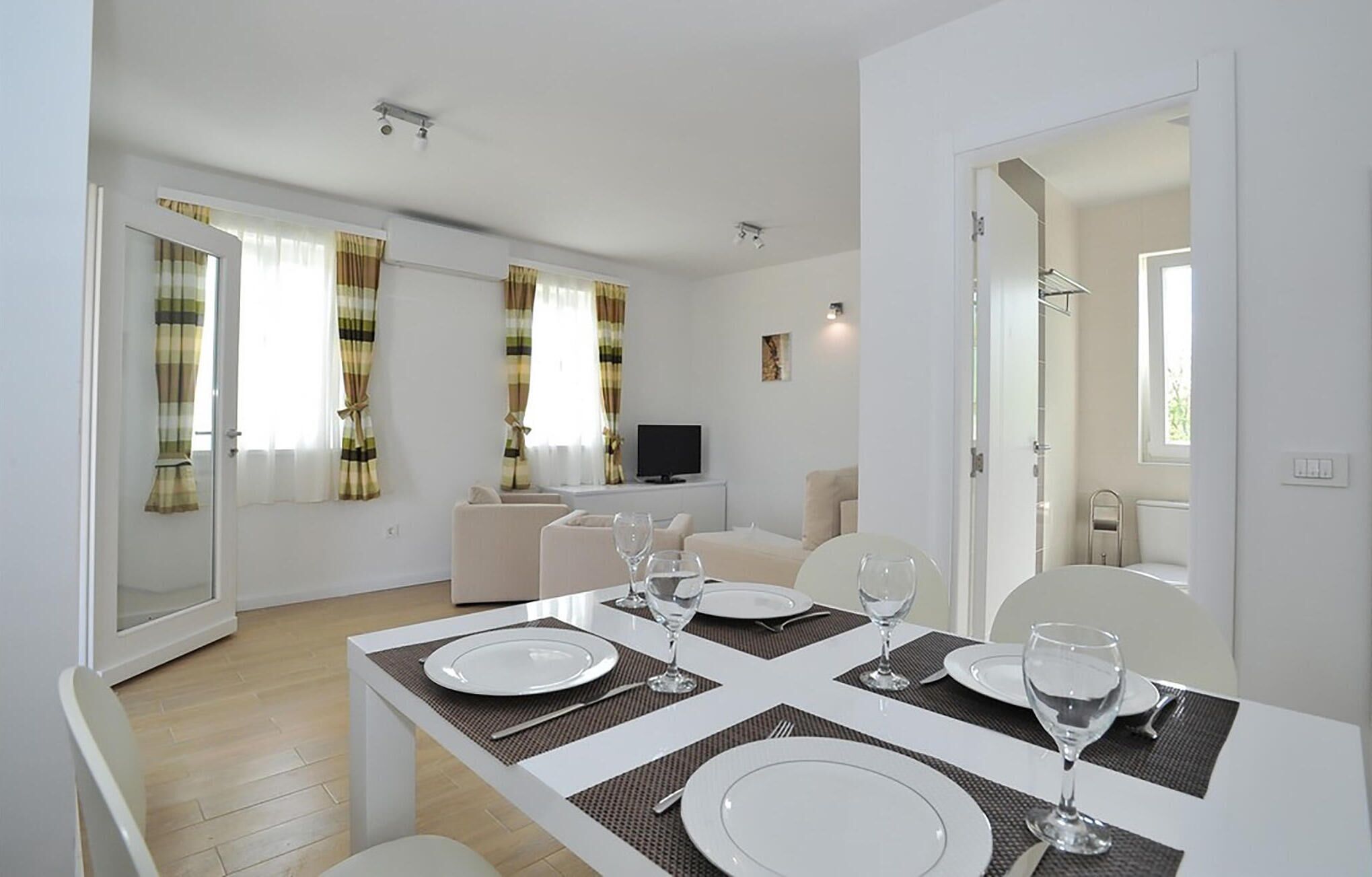 A modern dining area with a large table set for four, a sofa, and a television in the background.