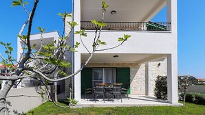 Ein modernes, zweistöckiges Gebäude mit einem Balkon, einem Essbereich mit Stühlen und einem Tisch sowie einer Steinwand.
