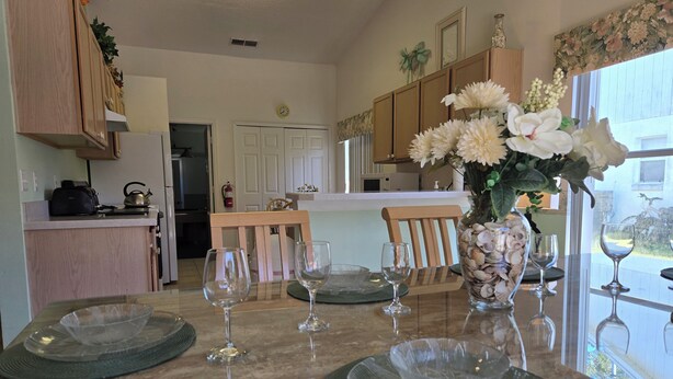 A kitchen with wooden cabinets, a dining table set with plates and wine glasses, and a vase with flowers. - Low Rates! Superb 4-bed Pool/Game Room Home Near Disney World Free Wi-fi & More (Kissimmee)