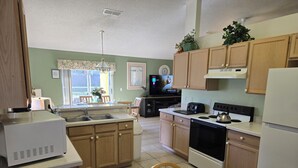 A kitchen with wooden cabinets, a built-in oven, a microwave, and a sink. There is a dining table with chairs and a vase of flowers. - Low Rates! Superb 4-bed Pool/Game Room Home Near Disney World Free Wi-fi & More (Kissimmee)