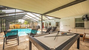 Ein Billardtisch, Stühle, ein Pool und eine überdachte Sitzgelegenheit mit Ventilator.