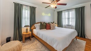 Ein ordentlich eingerichtetes Schlafzimmer mit einem Bett, Nachttischen, einer Lampe und einem Deckenventilator.