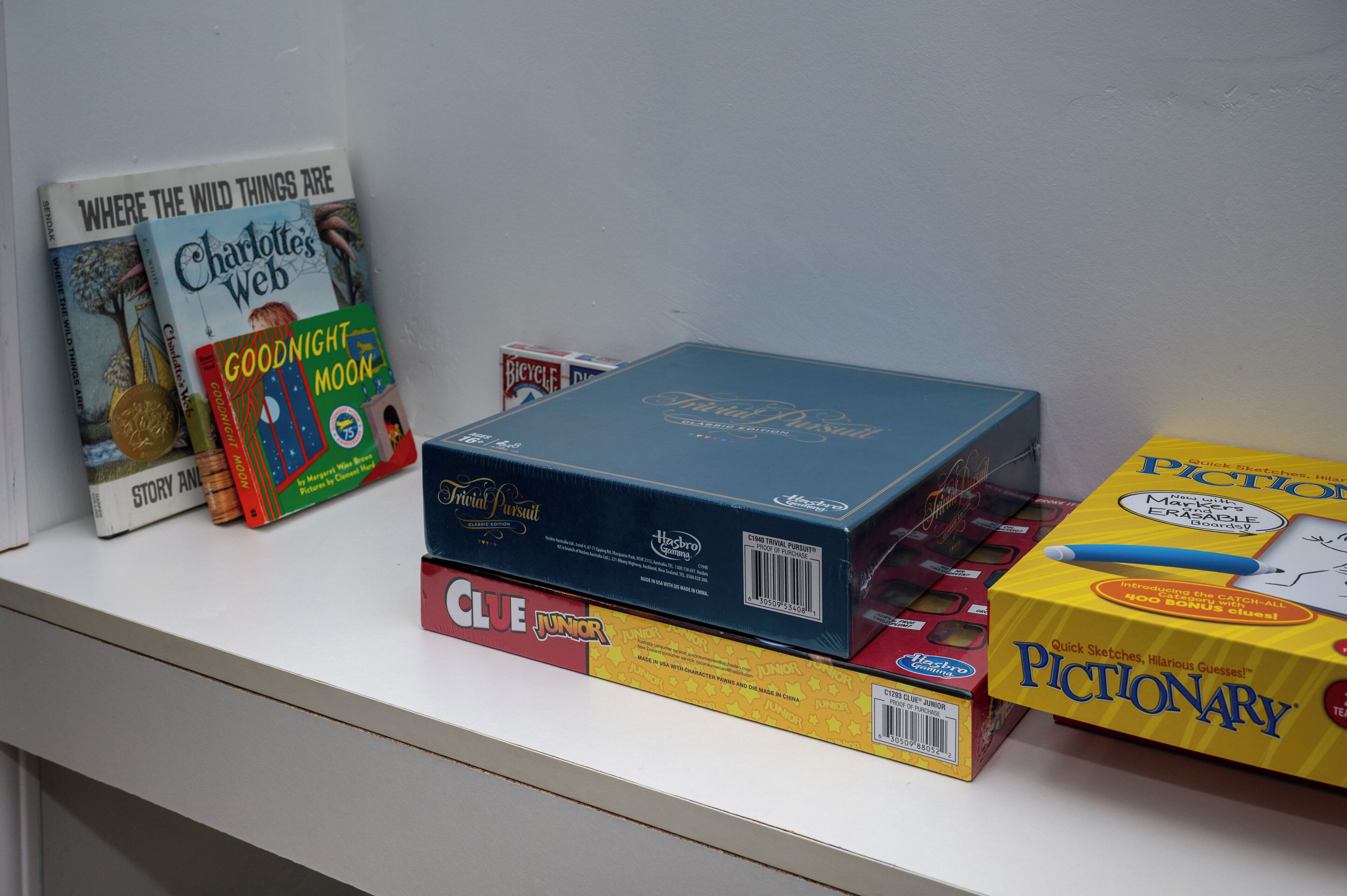 Una estantería con libros y juegos, incluyendo 'Charlotte's Web', 'Goodnight Moon' y 'Pictionary'.