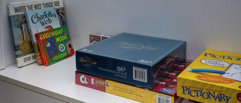Una estantería con libros y juegos, incluyendo 'Charlotte's Web', 'Goodnight Moon' y 'Pictionary'.