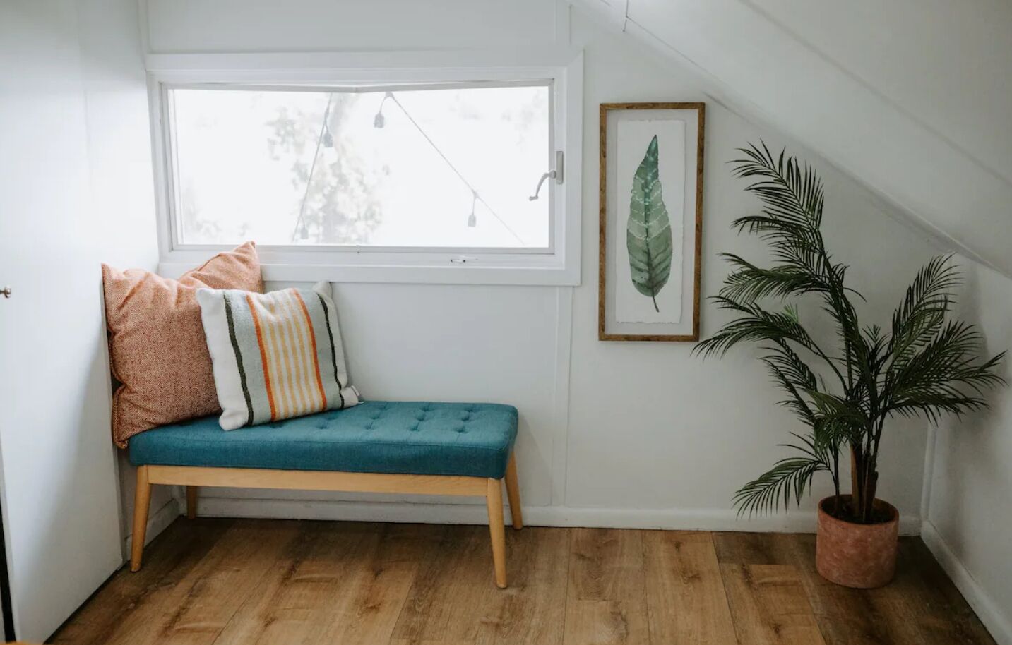 A cozy corner with a teal bench, a potted plant, and a framed leaf artwork.