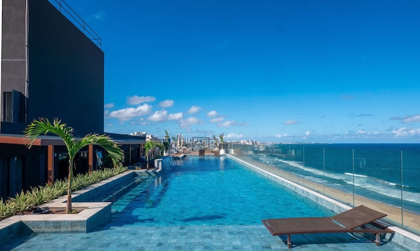 Ein Rooftop-Endlospool mit Blick auf das Meer, umgeben von Palmen und Liegestühlen.