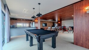Une table de billard dans un décor intérieur moderne, avec un coin cuisine visible à l’arrière-plan.