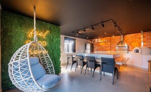 A modern kitchen with a hanging chair, a neon sign, and a brick wall. - Beachfront Building With Pool and gym - Arus (Salvador)