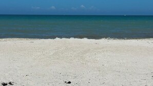 En strand med vit sand och stilla, blått vatten.