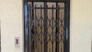 A black metal gate with a diamond pattern, a small electronic lock, and a textured beige wall.