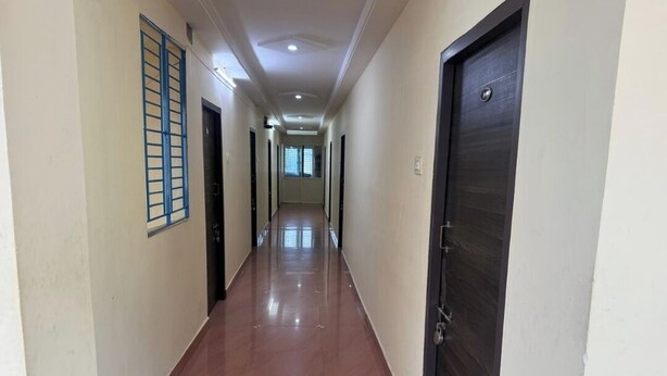A long, narrow hallway with a shiny floor, doors on both sides, and a window with blue bars on the left.