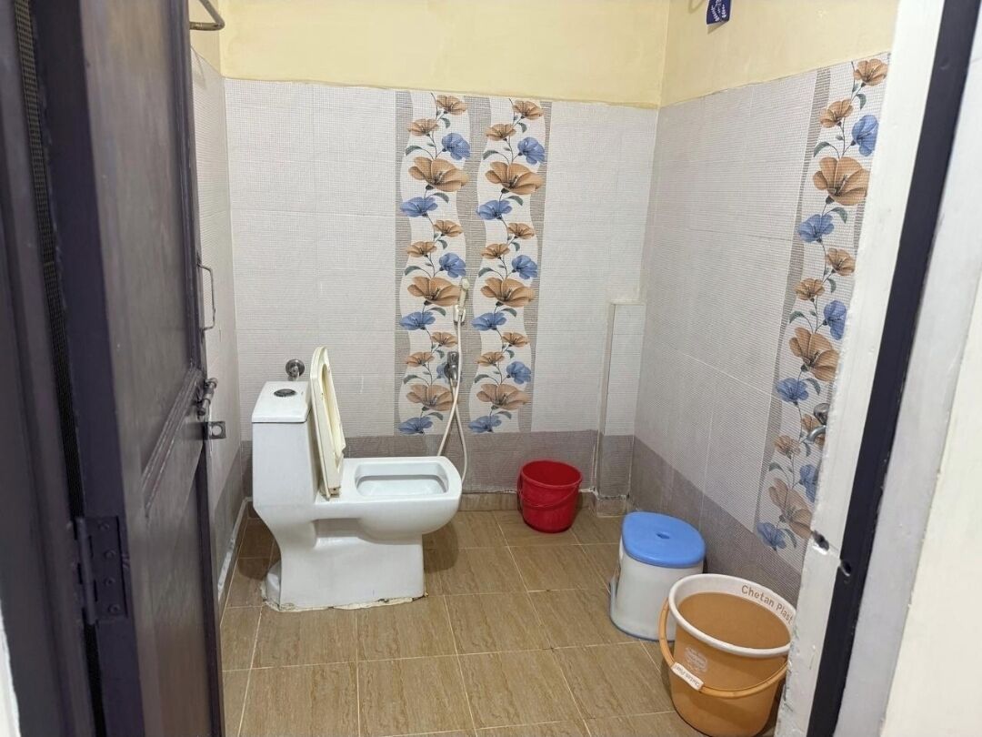 A small bathroom with a toilet, a red bucket, and a blue trash bin.