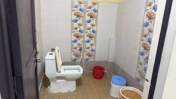 A small bathroom with a toilet, a red bucket, and a blue trash bin.