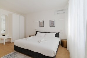 Una habitación de hotel moderna con una cama grande, un espejo, una mesita auxiliar pequeña y dos cuadros en la pared.