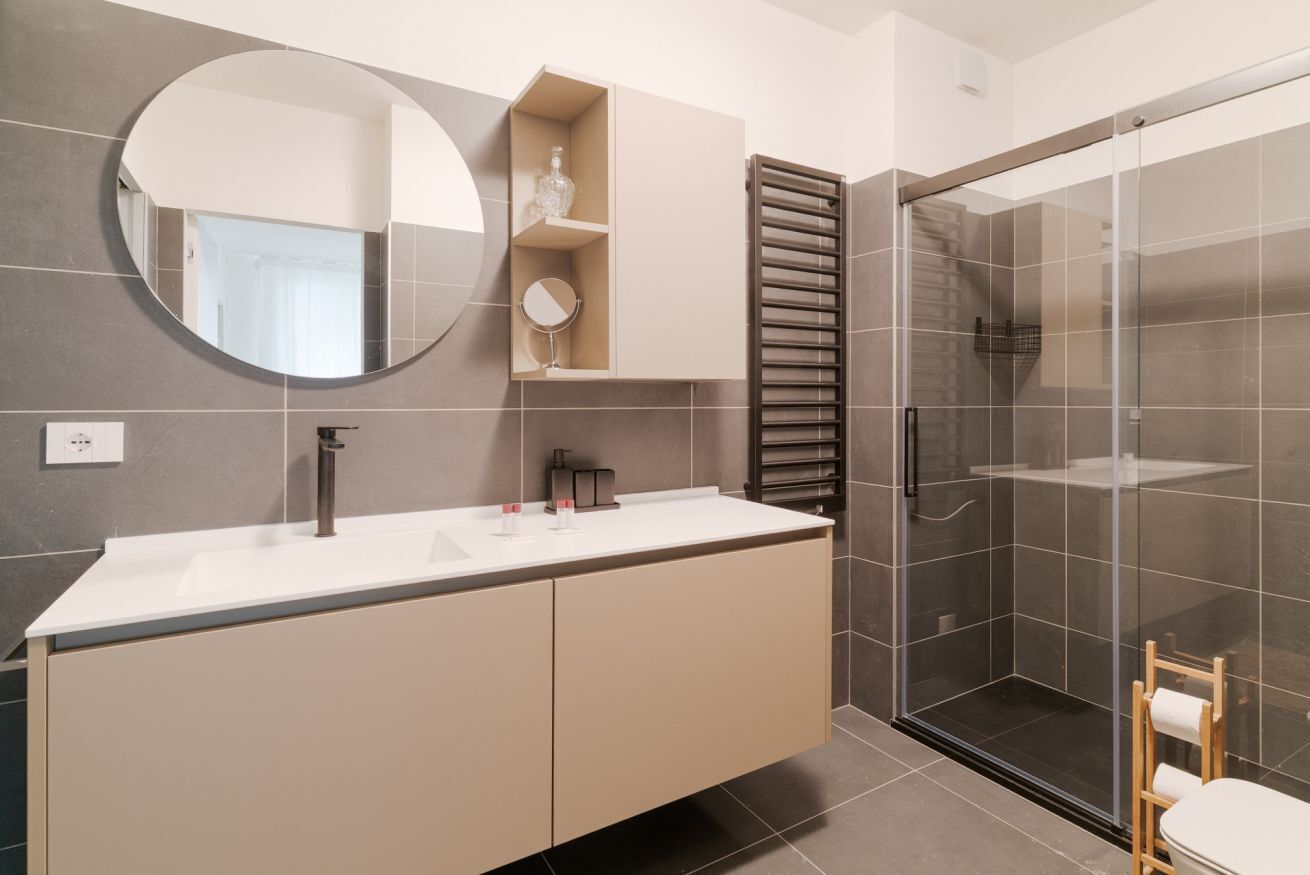 Un baño moderno con un espejo grande, un lavabo, una ducha con mampara de vidrio y un perchero para toallas.