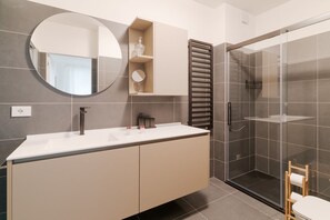 Un baño moderno con un espejo grande, un lavabo, una ducha con mampara de vidrio y un perchero para toallas.