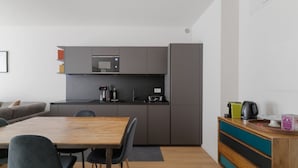 Une cuisine moderne avec des meubles gris, un four à micro-ondes et une machine à café. On y trouve une table à manger en bois avec des chaises.
