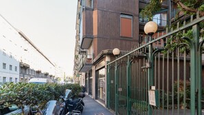 Une rue étroite en milieu urbain, avec un bâtiment agrémenté d’une clôture en métal et d’une plaque indiquant le numéro de l’immeble.