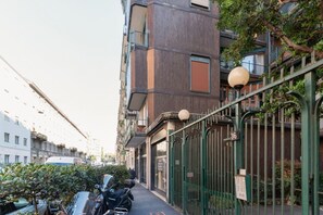 Una calle estrecha en la ciudad con un edificio que tiene una cerca metálica y un cartel con un número.