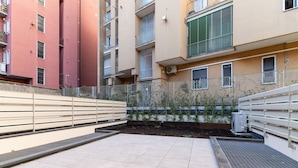 Une cour avec un sol carrelé, une clôture en métal et un bâtiment doté de nombreux balcons et fenêtres.