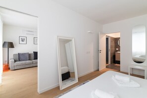 Una habitación de hotel moderna con cama, espejo, sofá y baño visible a través de una puerta abierta.