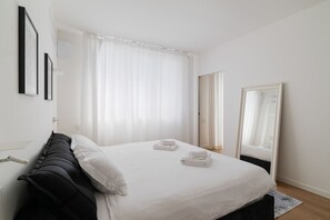 Una habitación de hotel con una cama, cortinas blancas, un espejo y una puerta.